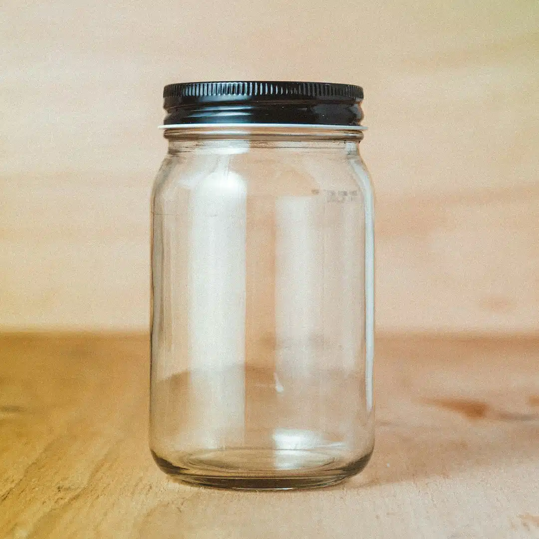 De kunst van het niet weten An empty glass jar with a black metal lid on a wooden surface